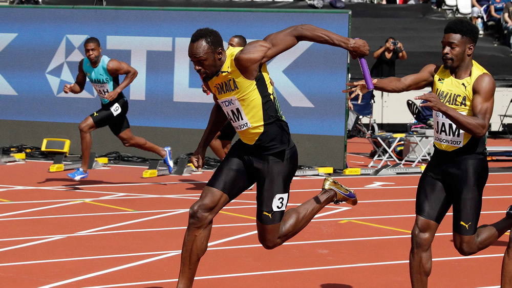 Usain Bolt přebírá štafetu v plné rychlosti ve finále běhu na 4x100 metrů na mistrovství světa v atletice 2017